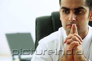 PictureIndia - Businessman with hands clasped, fingers on mouth, looking away