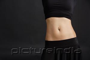 PictureIndia - Woman's mid section with belly button ring, black background