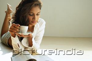 PictureIndia - Woman looking at magazine, holding cup and saucer