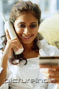 PictureIndia - Woman using cordless phone and looking at credit card