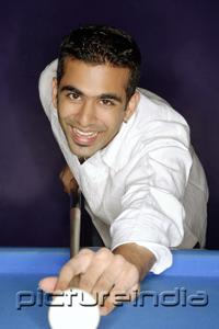 PictureIndia - Young man playing pool, smiling at camera
