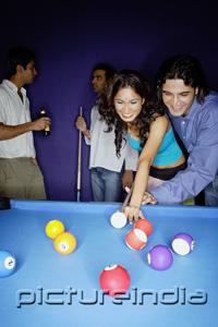 PictureIndia - Young adults playing pool, man teaching woman to aim