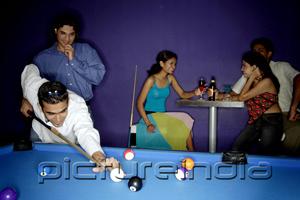 PictureIndia - Young adults playing pool, people in the background having beer