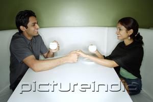 PictureIndia - Couple sitting opposite from each other, having tea, holding hands