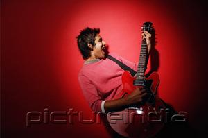 PictureIndia - Young man with guitar, standing against red background