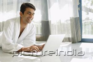 PictureIndia - Man in bathrobe, lying on floor, using laptop