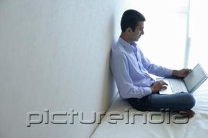 PictureIndia - Man sitting on bed, using laptop