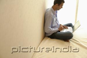 PictureIndia - Man sitting cross-legged on bed, using laptop