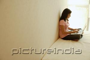 PictureIndia - Woman at home, sitting on bed, using laptop