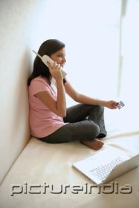 PictureIndia - Woman at home, sitting on bed with laptop, using cordless phone
