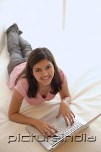 PictureIndia - Woman at home, lying on bed, using laptop