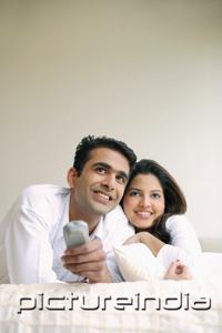 PictureIndia - Couple lying on bed, side by side, watching TV