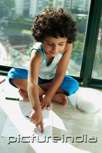 PictureIndia - Girl sitting on floor with crayons and paper, pointing to drawing