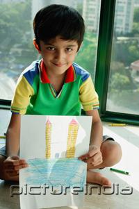 PictureIndia - Boy sitting on floor, holding a drawing towards camera