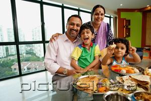 PictureIndia - Family of four sitting around dining table, smiling at camera