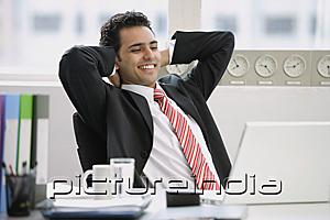 PictureIndia - Businessman sitting in office, hands behind head, smiling