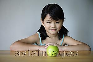 Asia Images Group - Little girl at table looking at green apple
