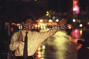 Asia Images Group - Male executive hailing taxi with umbrella in rain at night