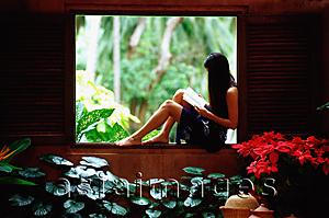 Asia Images Group - Woman sitting on window ledge, reading