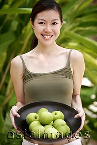 Asia Images Group - Young woman looking at camera, holding a bowl of apples