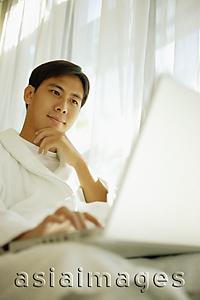 Asia Images Group - Young man using laptop, focus on the background