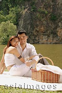 Asia Images Group - Couple sitting by a lake, with picnic basket, looking at camera