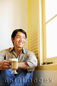 Asia Images Group - Man sitting next to window holding mug of coffee