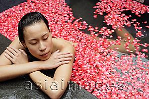 Asia Images Group - Woman leaning at edge of tub, flowers floating in water