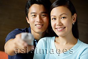 Asia Images Group - Couple side by side, man holding TV remote control towards camera
