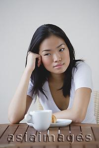 Asia Images Group - Young woman leaning head on hand, cup and saucer on table