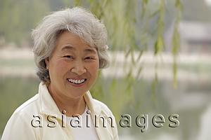 Asia Images Group - Head shot older woman smiling beneath a tree