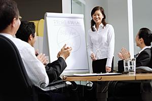 AsiaPix - Businesswoman standing next to flipchart, colleagues sitting and clapping