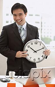 AsiaPix - Businessman standing in front of desk, holding clock