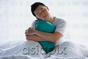 AsiaPix - Man sitting in bed, embracing pillow