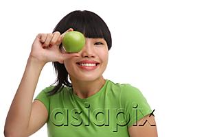 AsiaPix - Young woman in green T-shirt holding green apple over eye