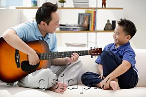 AsiaPix - Father and son sitting on sofa, father playing guitar