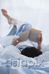 AsiaPix - Young woman lying in bed, reading a book