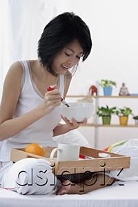 AsiaPix - Young woman sitting on bed, having breakfast